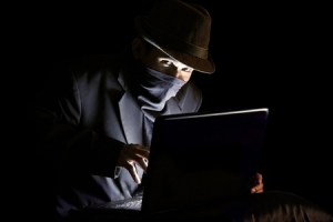 Masked man in the dark looking sinister in front of a laptop